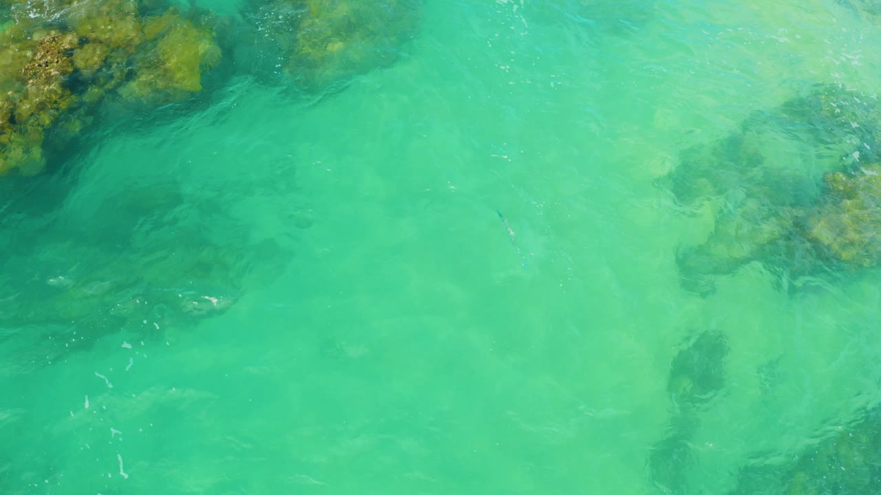 Turquoise shallow water with submerged reef rocks near the top edge.