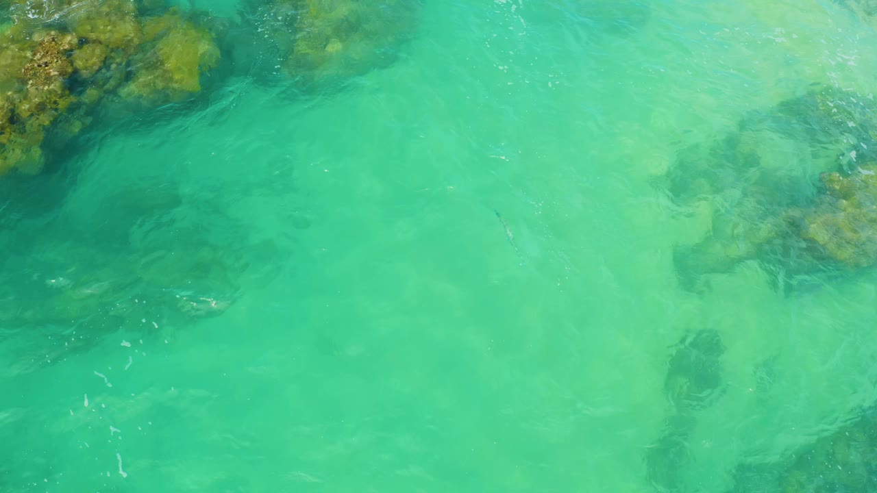 Green shallow water passes over reef formations at Laguna Beach, Baja California Sur, with a darker submerged patch below center and no visible people.