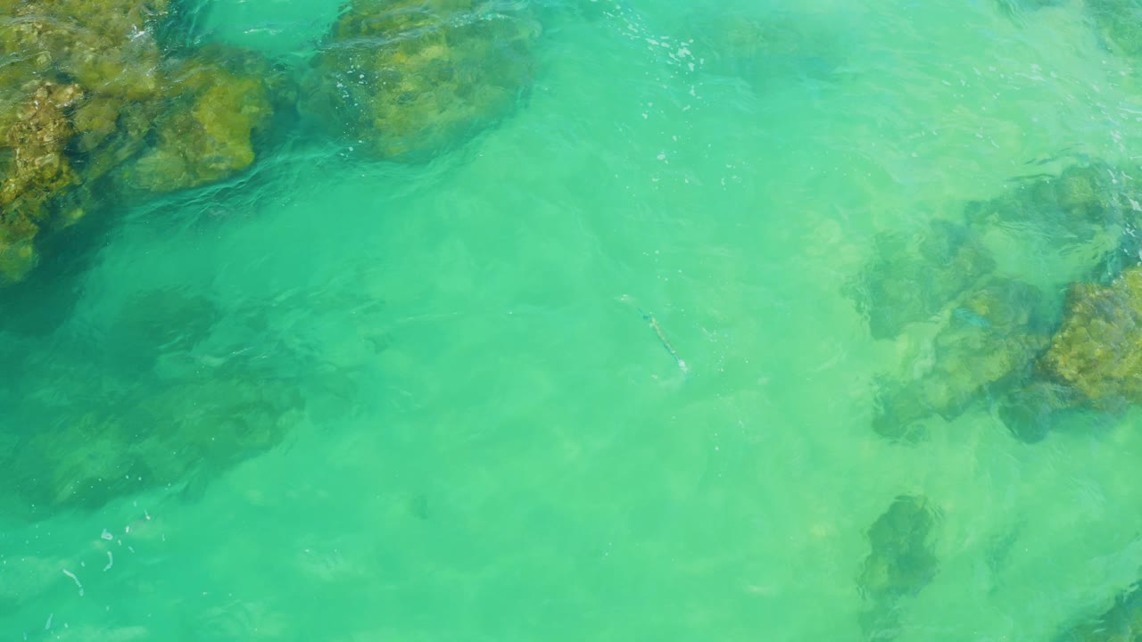 Top-down view of Laguna Beach, Baja California Sur water with reef rocks at the upper left, darker submerged reef at lower left, and no visible people.