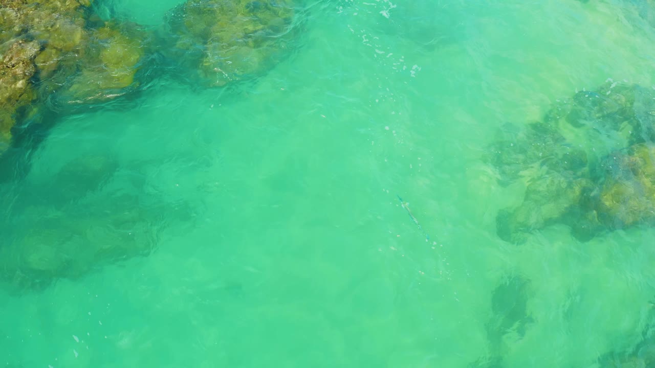 Clear green-blue sea covers submerged rock formations near the top edge at Laguna Beach, Baja California Sur, with no visible people.
