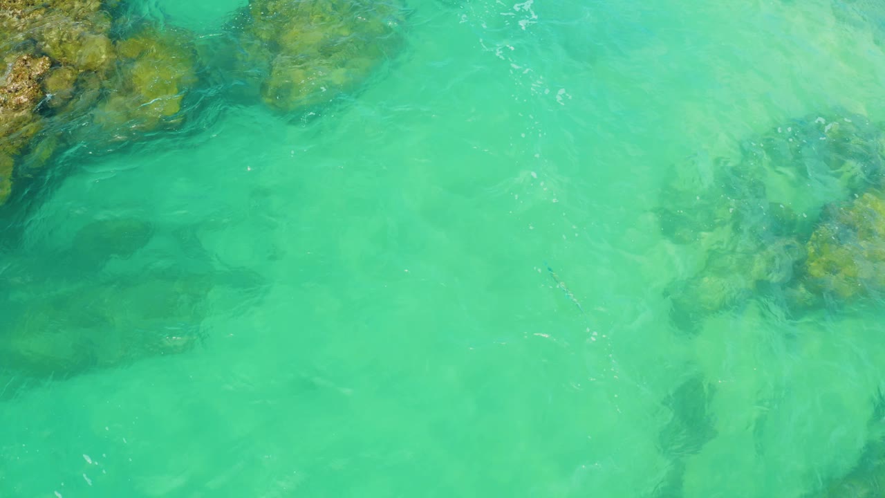 Turquoise shallows show darker rock shadows and pale sand beneath the water at Laguna Beach, Baja California Sur, with no visible people.