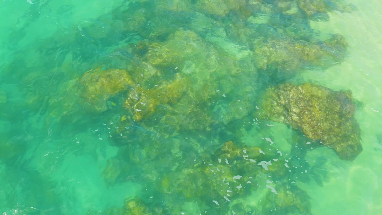 Overhead view of turquoise water and submerged tan rocks at Laguna Beach, Baja California Sur, with no visible people.