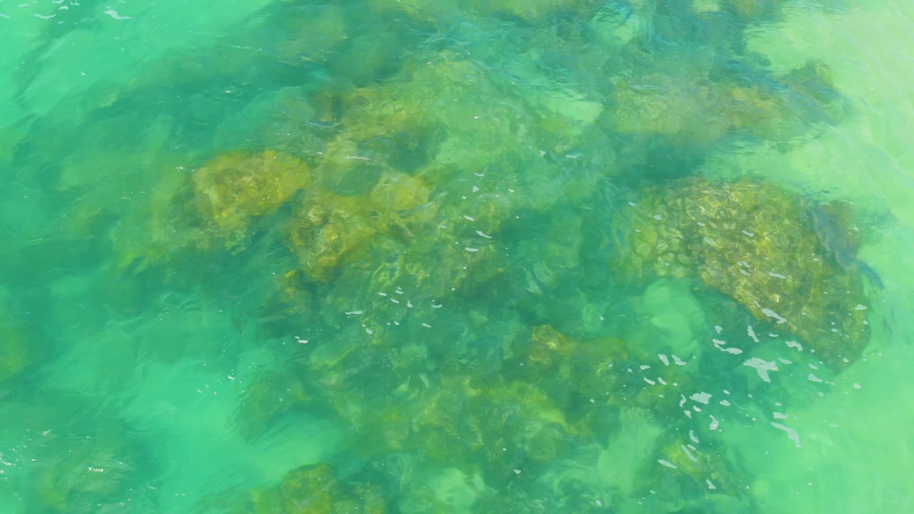 Bright lagoon water reveals darker submerged rocks and tan patches at Laguna Beach, Baja California Sur, with no visible people.
