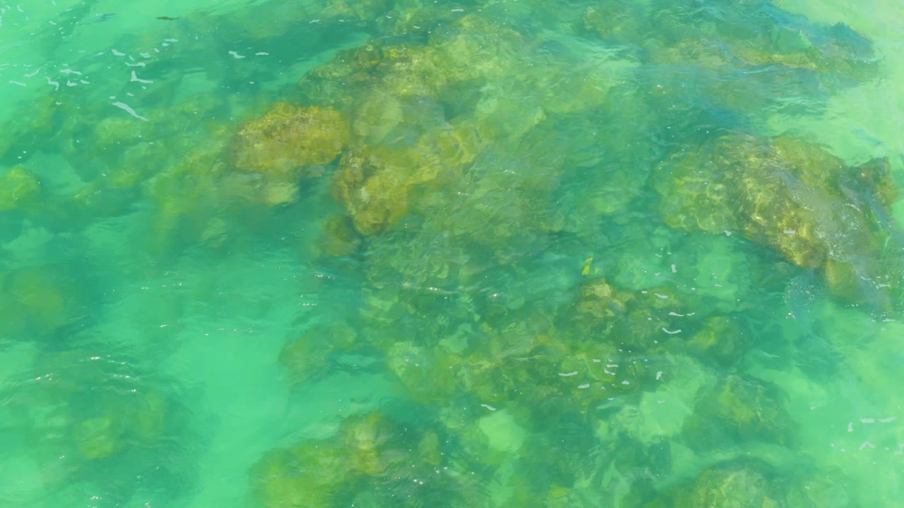Bright turquoise shallows reveal larger submerged rock shapes near the center of the frame in Laguna Beach, Baja California Sur, Mexico, with no visible people.