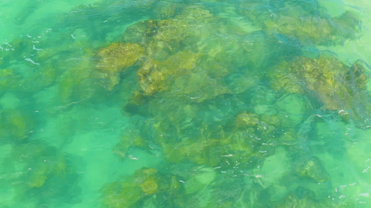 An overhead view shows clustered underwater rocks softened by rippled turquoise water at Laguna Beach, Baja California Sur, Mexico, with no visible people.