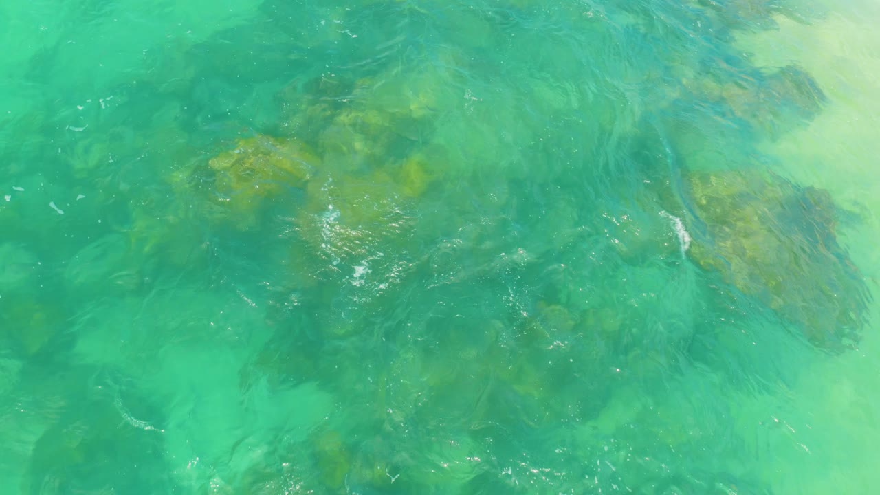 Shallow turquoise water at Laguna Beach, Baja California Sur shows darker reef patches spread across the frame, with faint ripples and no visible people.