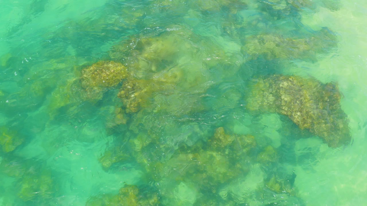 Overhead view of clear turquoise seawater covering brown submerged rocks at Laguna Beach, Baja California Sur, with no visible people.