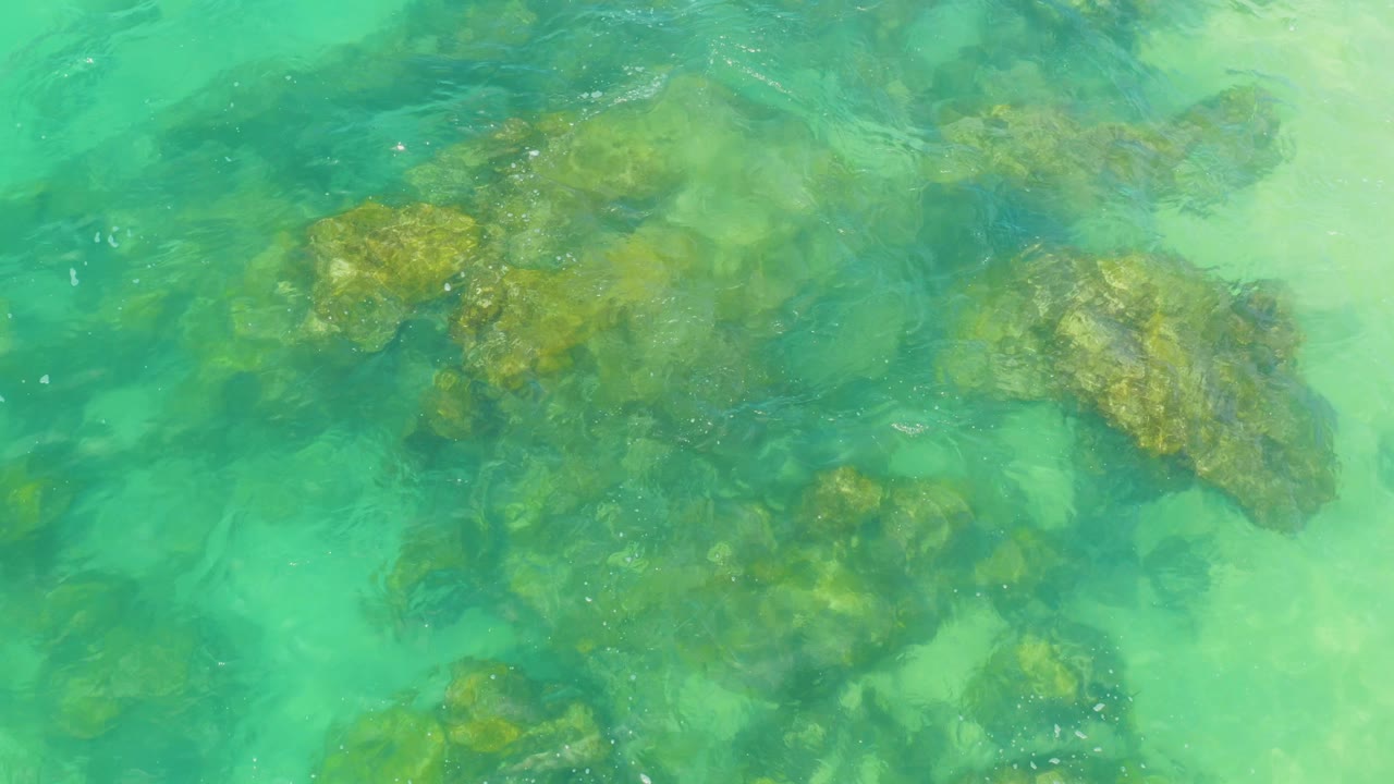 Shallow turquoise sea viewed from above in Laguna Beach, Baja California Sur, with submerged rocks softened by surface ripple and no visible people.