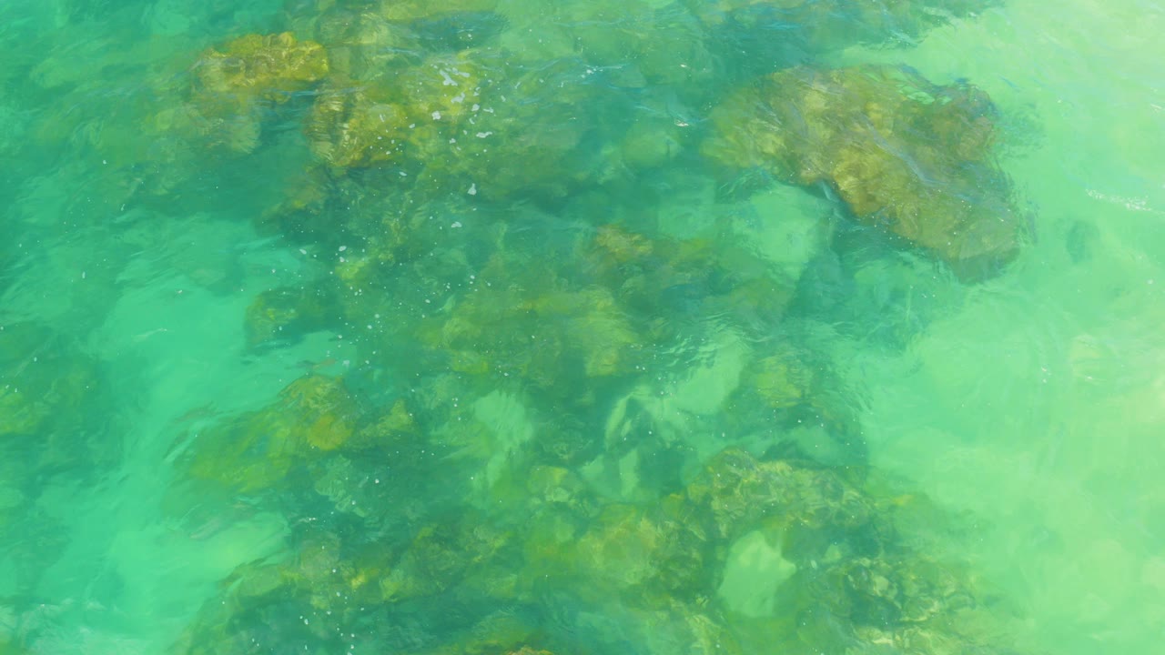 Top-down view of turquoise ocean water over dark and brown submerged rocks in Laguna Beach, Baja California Sur, with no visible people.