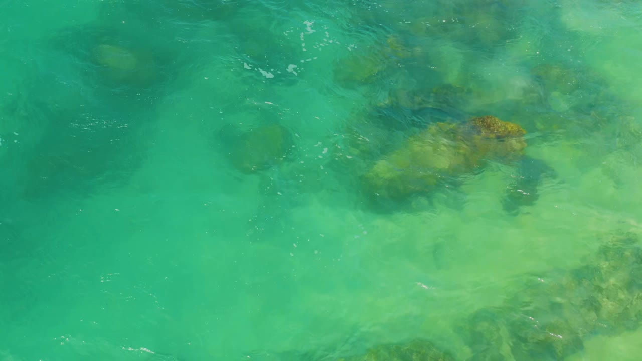 Top-down view of turquoise ocean water over dark submerged rocks in Laguna Beach, Baja California Sur, with no visible people.