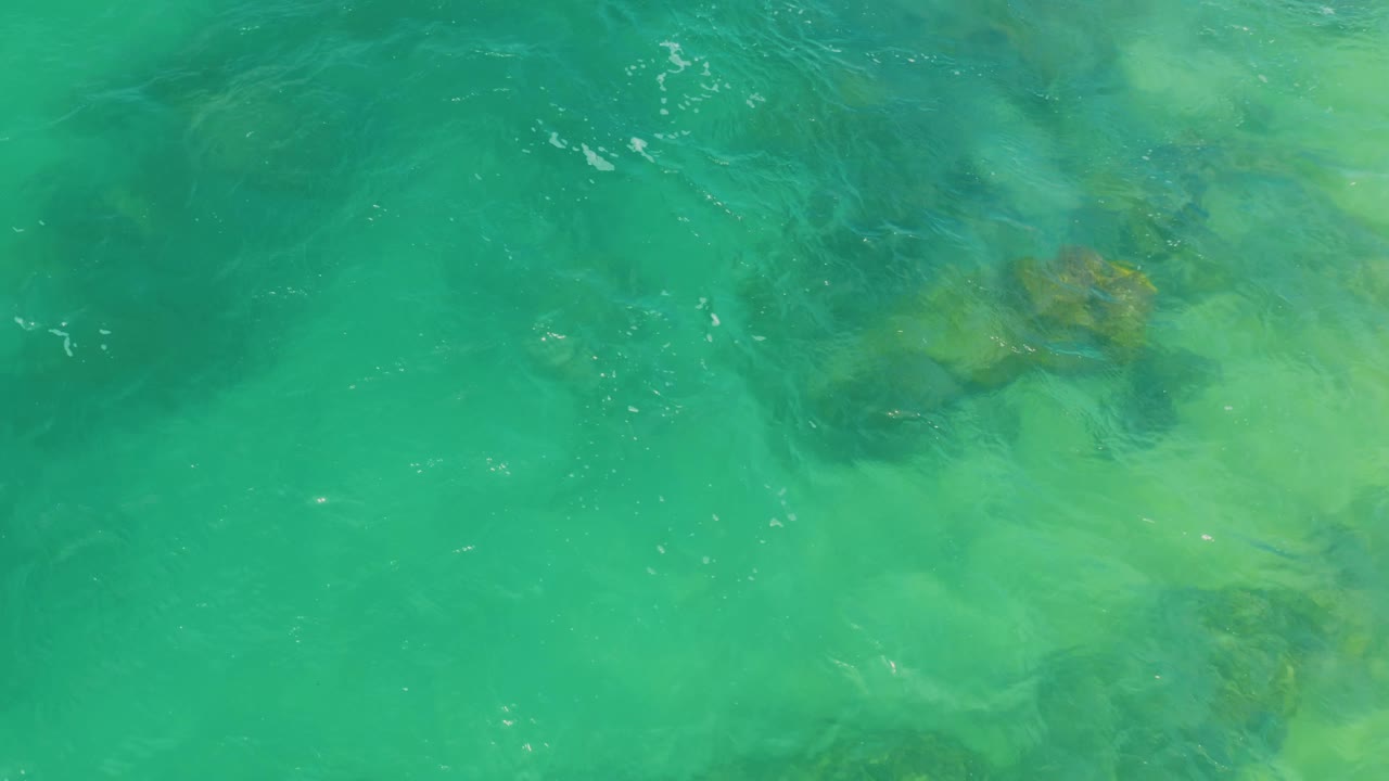 Ripples pass over submerged rocks and pale sand under turquoise water in Laguna Beach, Baja California Sur, with no visible people.