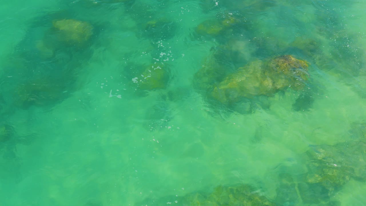 Top-down view of turquoise water over submerged rocks and pale sand in Laguna Beach, Baja California Sur, with no visible people.
