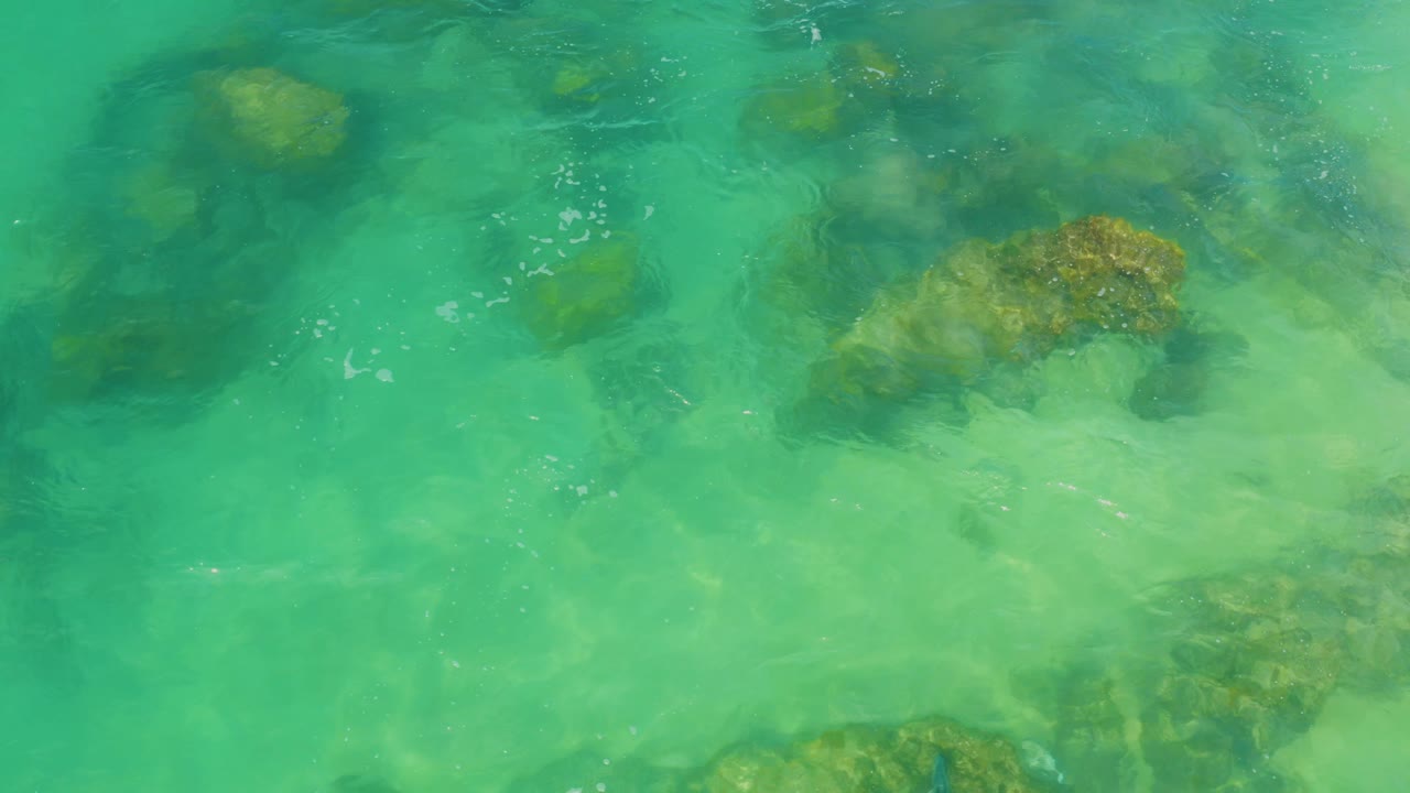 Shallow turquoise water reveals tan rocks and pale sand in Laguna Beach, Baja California Sur, with small surface bubbles and no visible people.