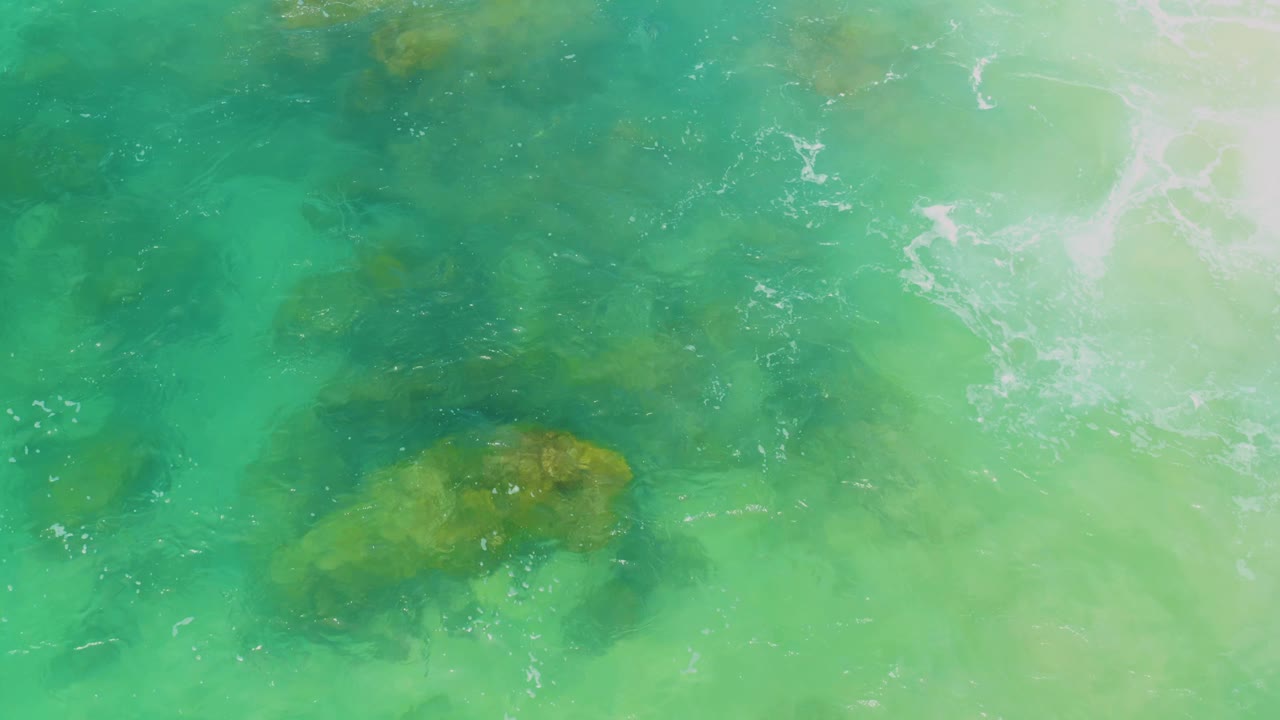 Clear green and turquoise seawater at Laguna Beach, Baja California Sur, showing a larger submerged rock form near the lower center and no visible people.