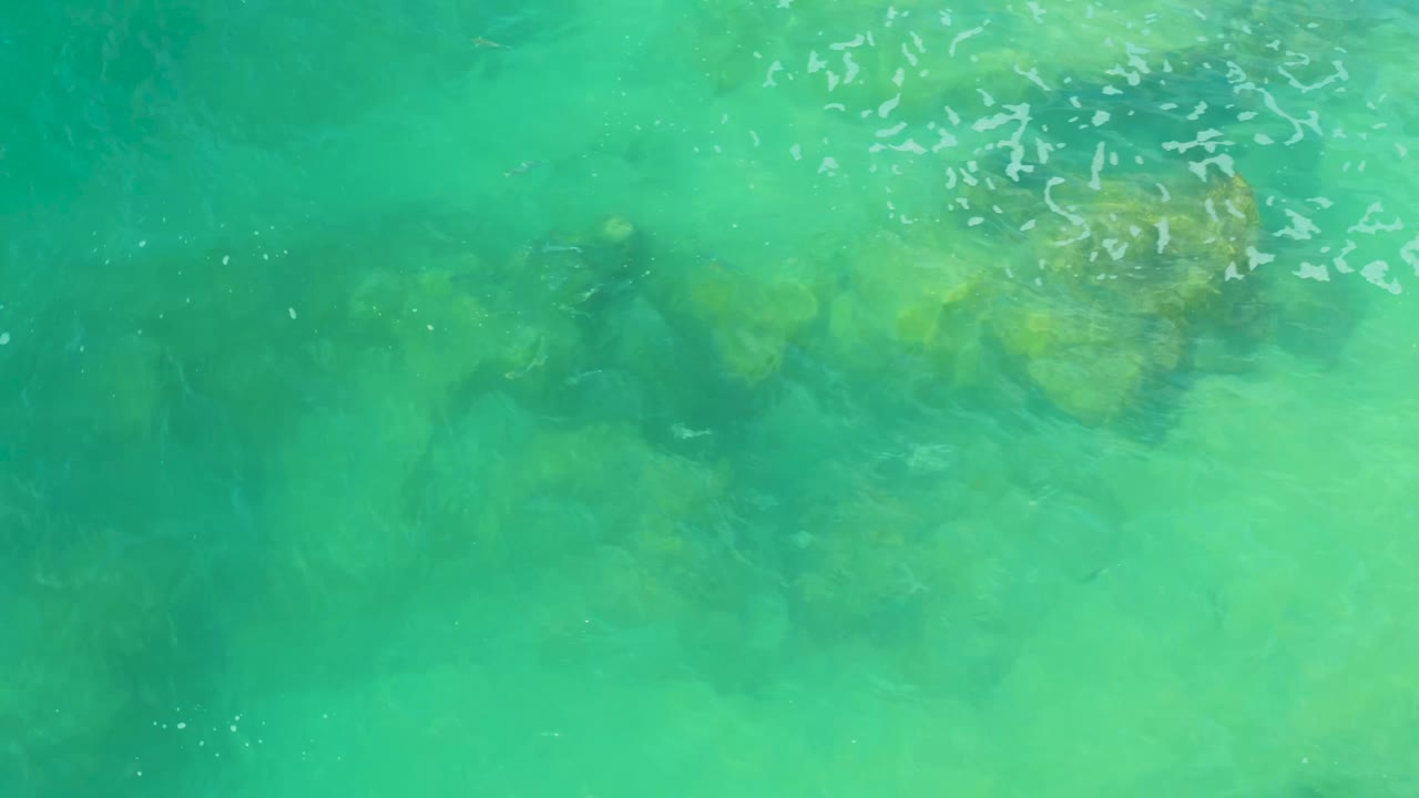 Green-blue coastal water at Laguna Beach, Baja California Sur, shows darker rock forms under soft surface ripples, with no visible people.