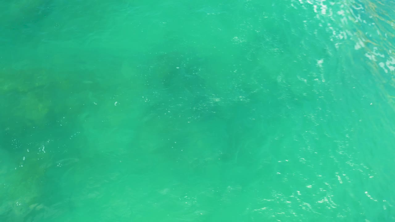Shallow water at Laguna Beach, Baja California Sur, fills the frame with a diagonal streak of reflected light and faint rocks below, with no visible people.