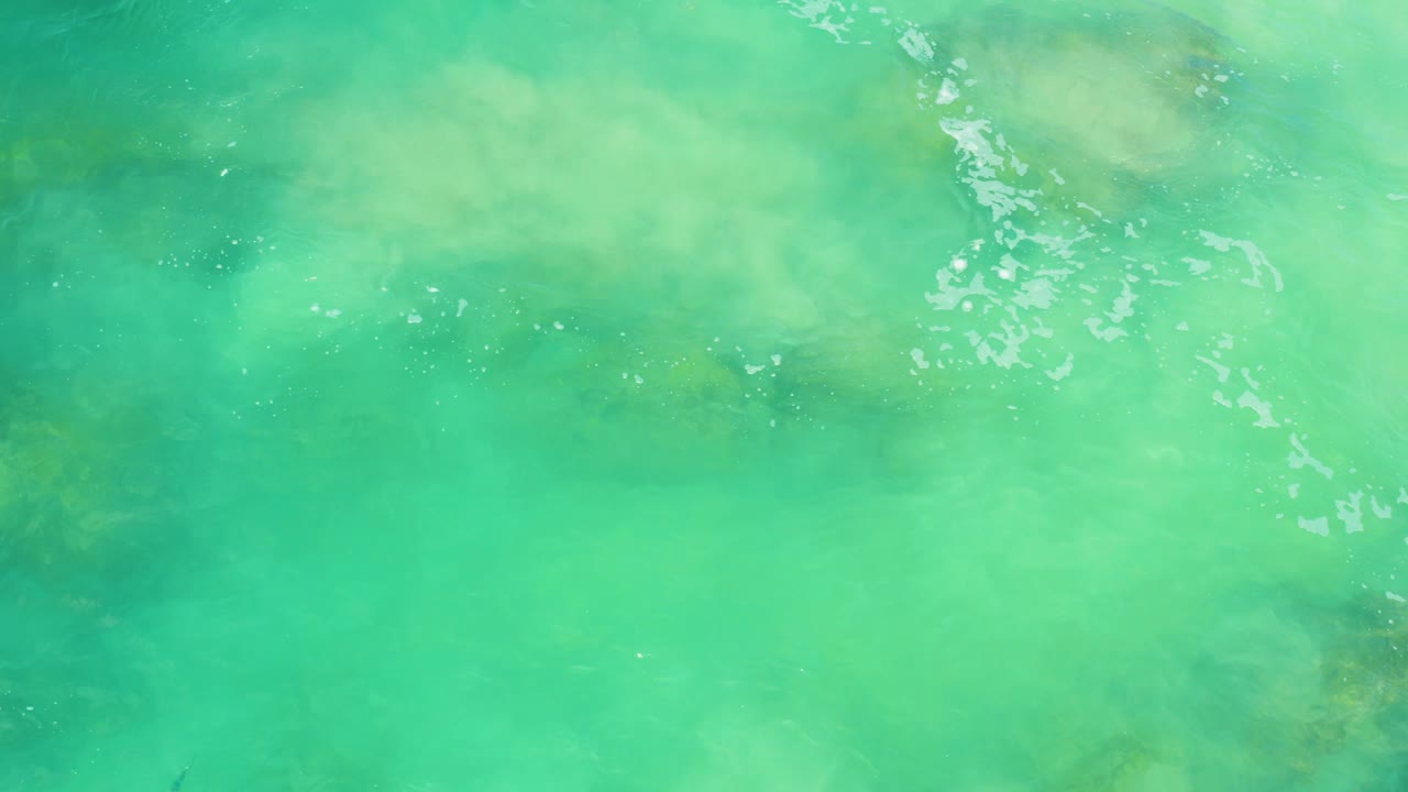 Shallow turquoise water reveals pale sediment and muted rock forms below the surface at Laguna Beach, Baja California Sur, with no visible people.