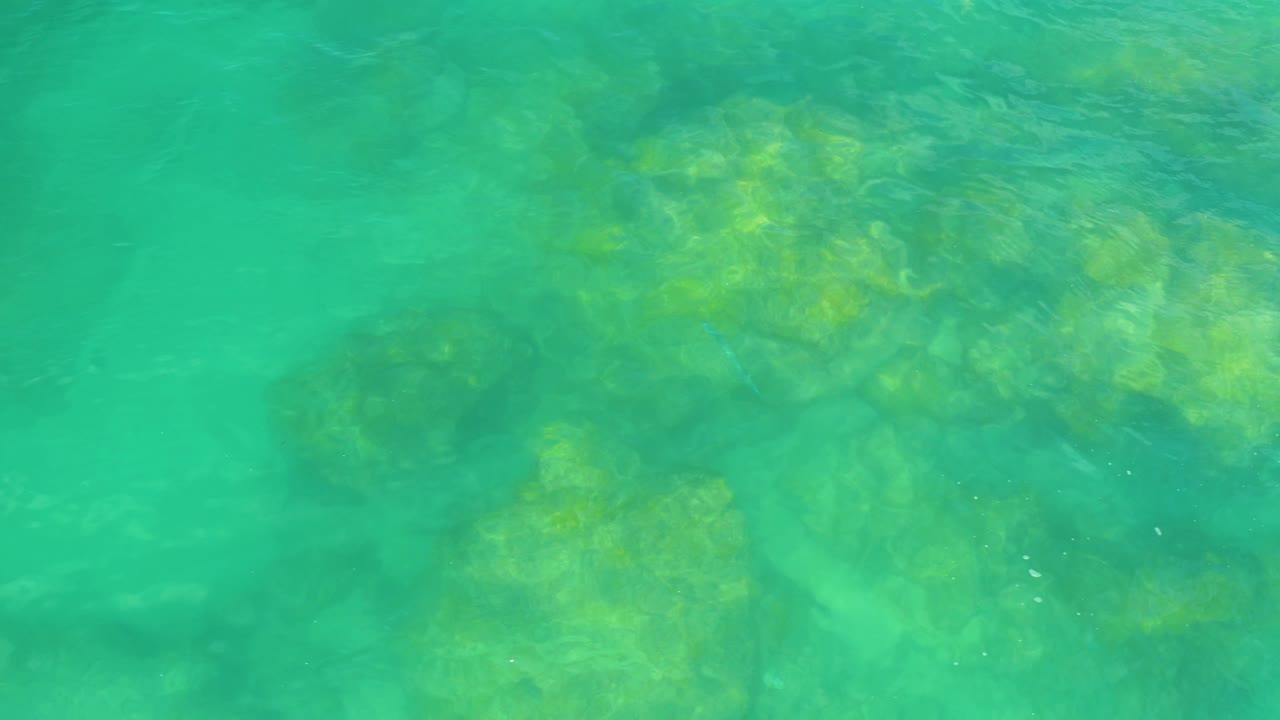 Shallow turquoise water in Laguna Beach, Baja California Sur, with blurred rock shapes appearing through the moving surface and no visible people.