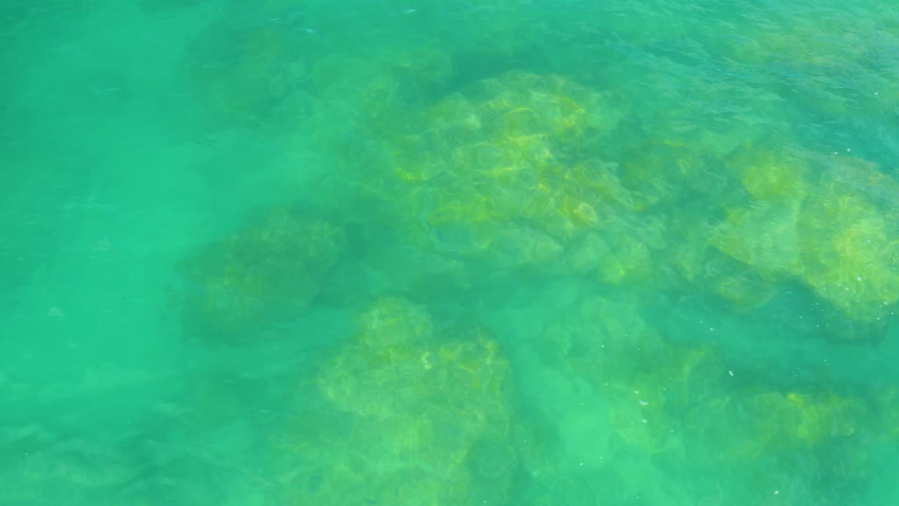 Clear green coastal water in Laguna Beach, Baja California Sur, with brighter rock patches visible under gentle ripples and no visible people.