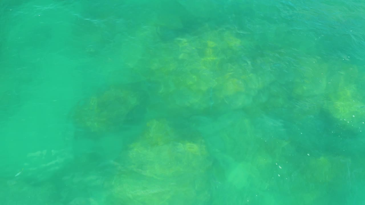 Green-blue ocean surface passes over muted rock shapes below the water at Laguna Beach, Baja California Sur, with no visible people.