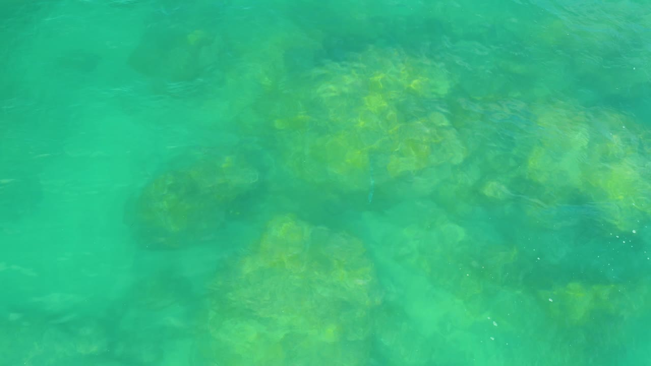 Clear turquoise sea reveals yellow-green rock patches under a lightly rippled surface at Laguna Beach, Baja California Sur, with no visible people.