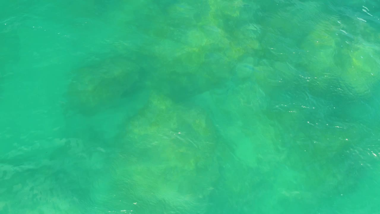 Overhead view of turquoise seawater with darker submerged rock patches visible near the upper half in Laguna Beach, Baja California Sur, with no visible people.