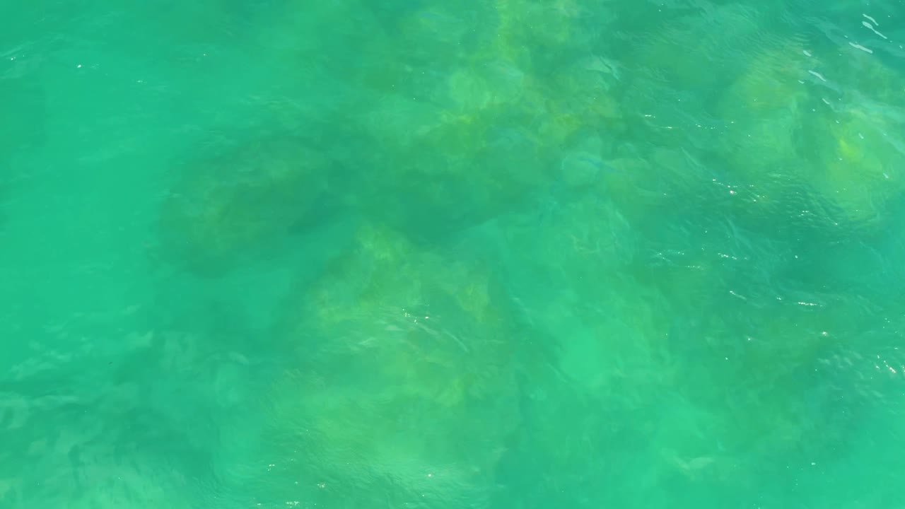 Aerial-looking frame of green-blue sea water over soft-edged underwater rocks in Laguna Beach, Baja California Sur, with small white ripple highlights and no visible people.