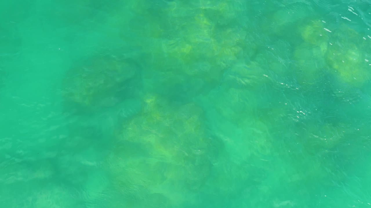 Turquoise water fills the frame with faint yellow-green rock forms below the surface in Laguna Beach, Baja California Sur, and no visible people or built objects.
