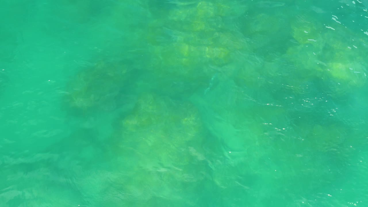 Overhead sea surface with ripples and darker submerged rocks showing through green water in Laguna Beach, Baja California Sur, with no visible people.