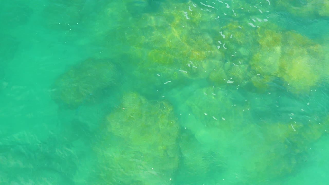 Turquoise shallow water over submerged rocks with small foam streaks.