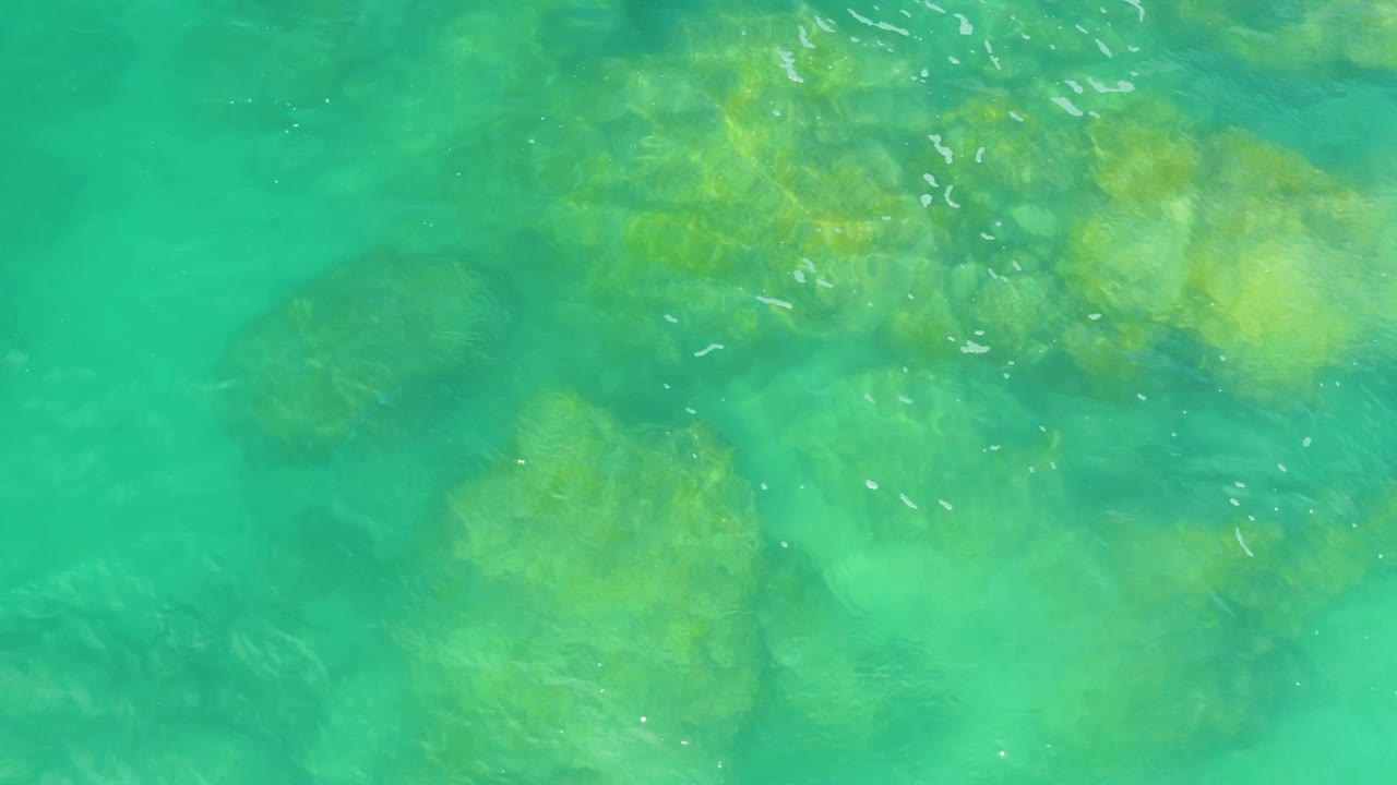 Overhead green-blue water in Laguna Beach, Baja California Sur, with pale submerged rock patches, thin foam marks near the upper area, and no visible people.