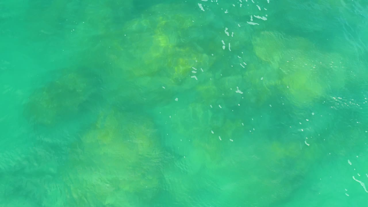 Turquoise-green water fills the frame, with pale yellow-green underwater variation and scattered reflected highlights, no visible people.