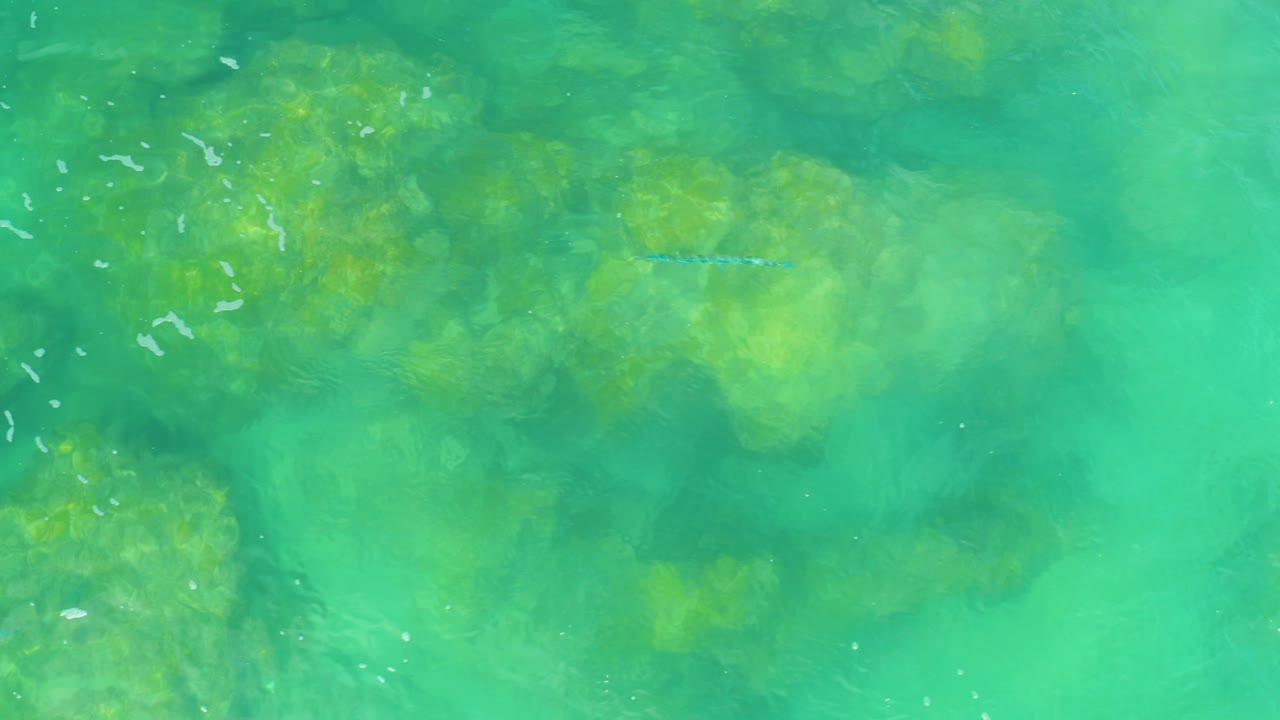 Top-down view of shallow turquoise sea at Laguna Beach, with broad soft-edged rock shadows below the surface and no visible people or vessels.