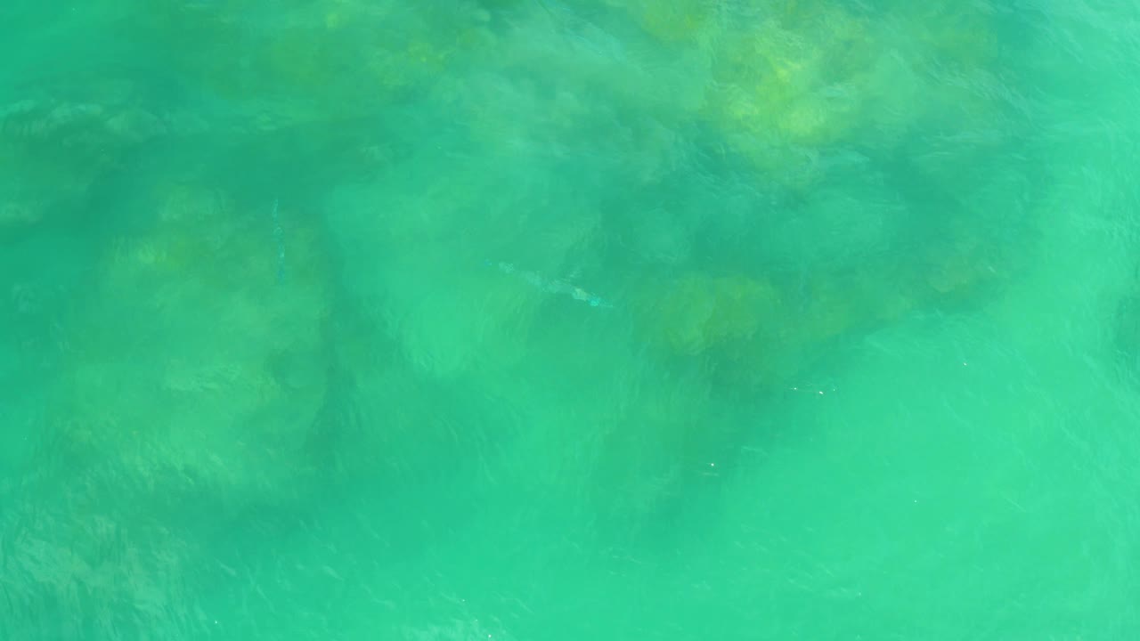 Overhead Laguna Beach water frame with diffuse submerged rocks visible through turquoise surface glare and no visible people.