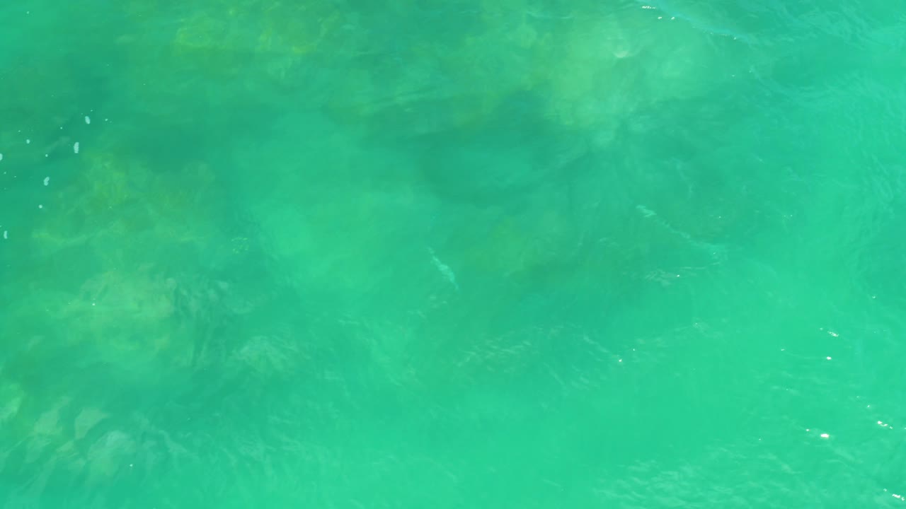 Aqua sea water at Laguna Beach, Baja California Sur, shows darker submerged rock forms under a lightly rippled surface, with no visible people.