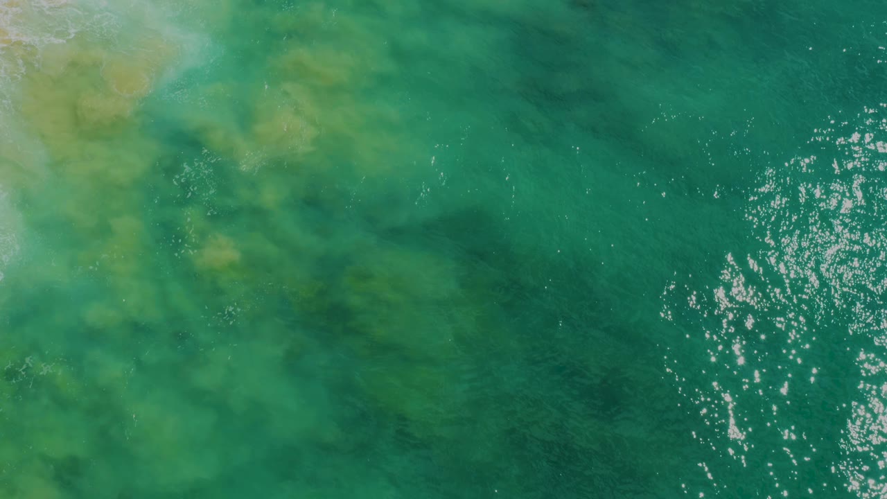 Aerial view of mottled green water with bright reflections on the right.