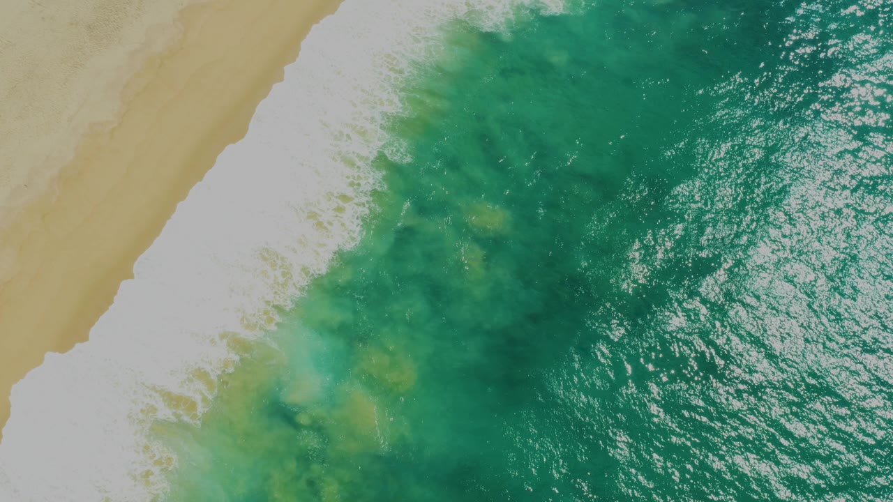 Overhead green surf breaking onto tan sand