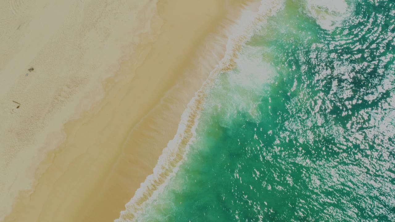 Overhead view of turquoise water and white foam meeting tan sand at Laguna Beach, Baja California Sur, with no visible people.