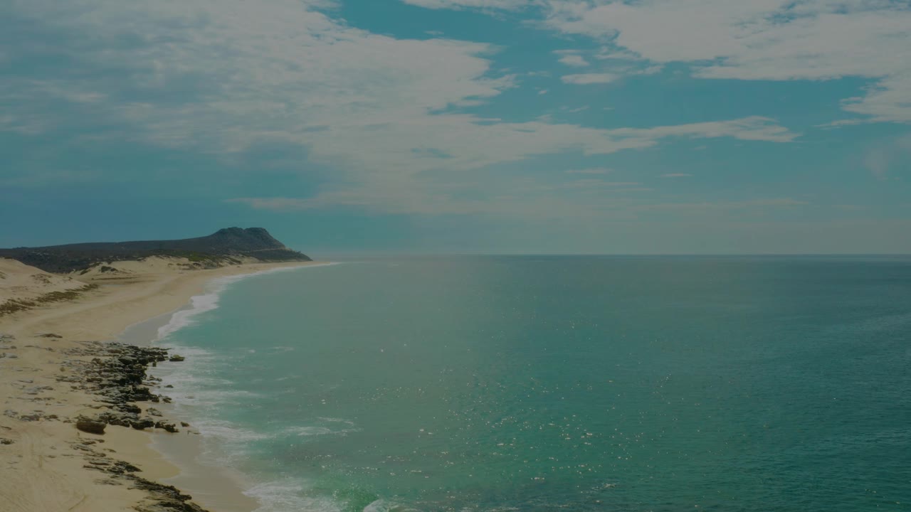 Curving beach beside turquoise water and dark rocks.