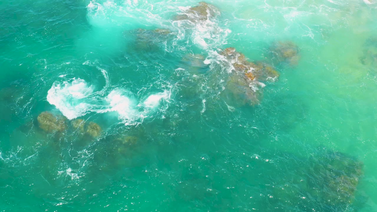 A white foam patch curls across green coastal water above scattered submerged rocks at Laguna Beach, Baja California Sur, with no visible people.