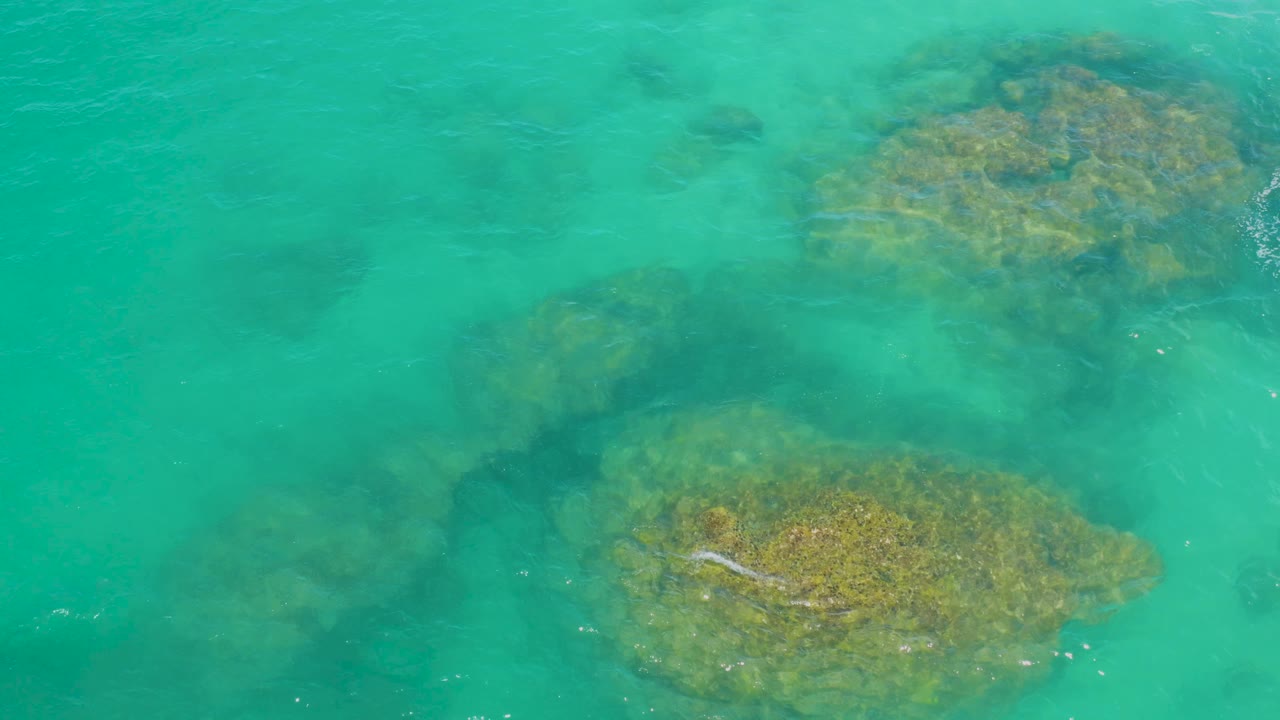 Top-down view of bright turquoise water at Laguna Beach, Baja California Sur, with a large reef patch near the lower frame and another near the upper right, with no visible people.