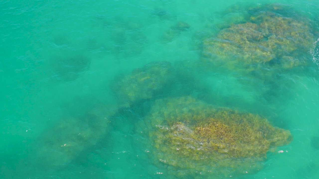 Overhead view at Laguna Beach, Baja California Sur, showing a reef patch low in frame and another near the top under green-blue water, with no visible people.