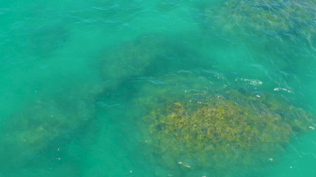 At 0:00, turquoise water in Laguna Beach, Baja California Sur ripples over beige-green submerged rocks, with no visible people.