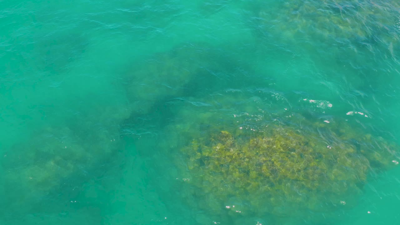 At 0:01, blue-green water covers a broad patch of submerged rock in Laguna Beach, Baja California Sur, with no visible people.