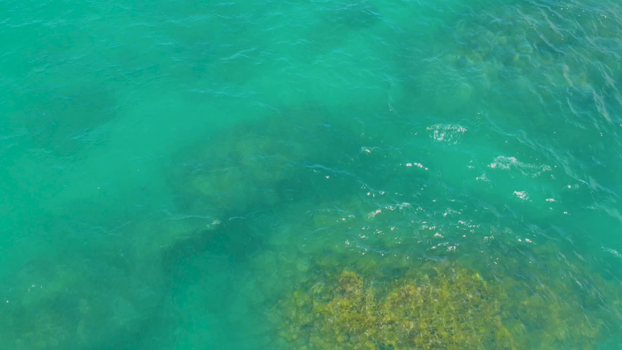At 0:03, teal water in Laguna Beach, Baja California Sur passes over darker submerged rock shapes and a few white glints, with no visible people.