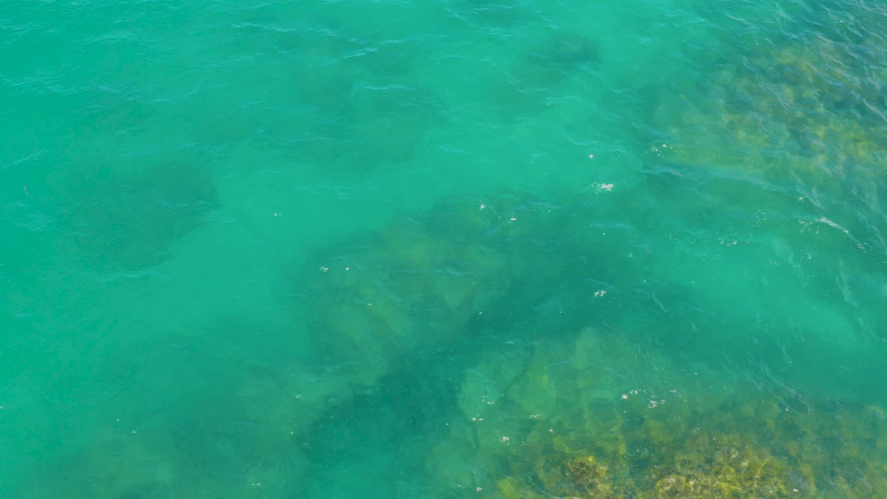Top-down view of turquoise ocean water at Laguna Beach, Baja California Sur, with dark submerged rock shapes and no visible people.