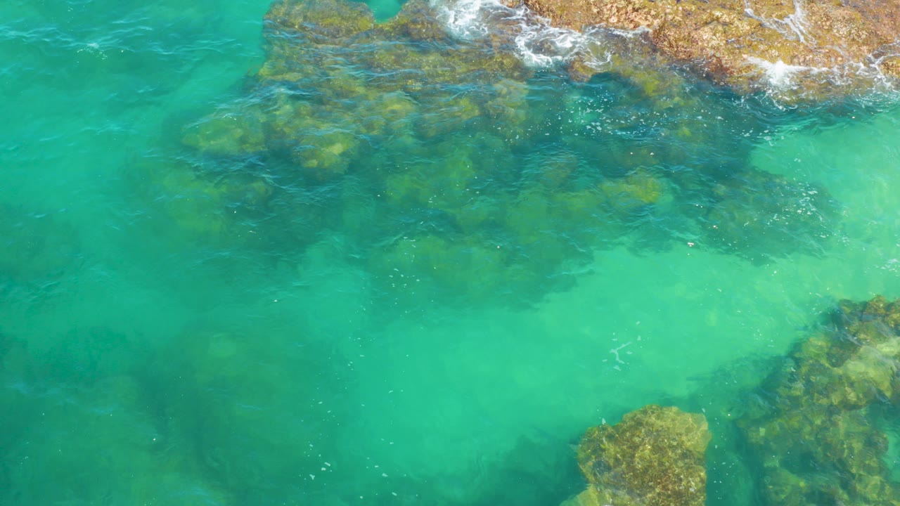 Top-down view of clear turquoise water over submerged rocks and pale sandy shallows at Laguna Beach, Baja California Sur, with no visible people.