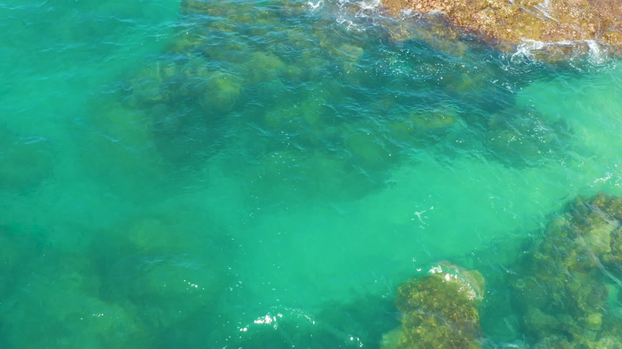 Transparent coastal water at Laguna Beach, Baja California Sur, shows submerged rock ledges along the top edge and lower right under gentle ripples, with no visible people.