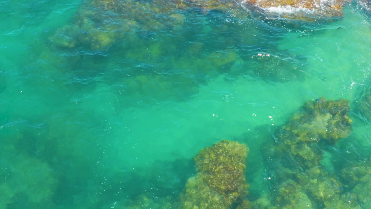 Overhead Laguna Beach water detail with turquoise shallows crossing darker underwater rocks and no visible people or structures.
