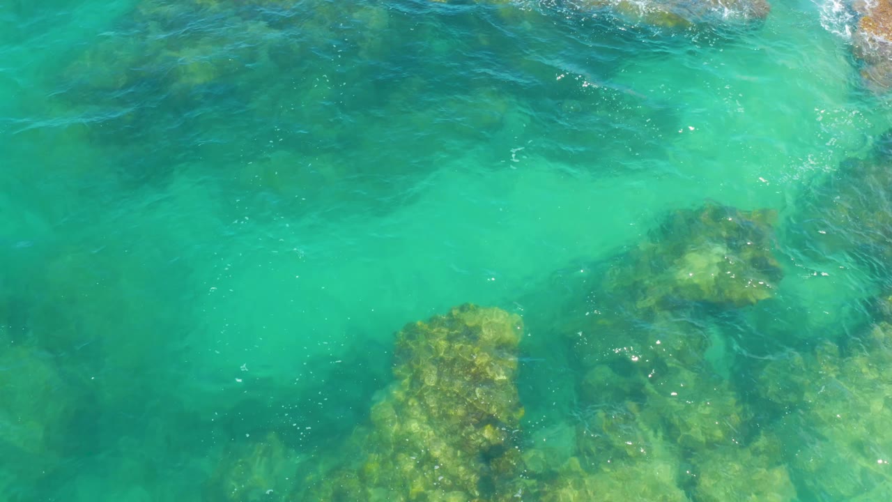 Sea green water ripples across submerged rock patches in Laguna Beach, Baja California Sur, with bright specks on the surface and no visible people.